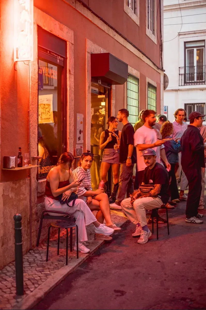 Friends sitting and standing outside the Palms Pizzeria shopfront in Lisbon at dusk